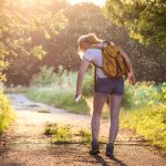 woman standing on path in woods surrounded by insects spraying herself with repellent